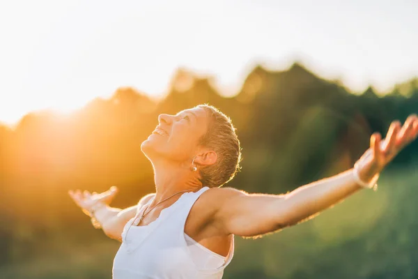 Female hormone therapy energy Energized and happy female with the sun shining behind her outside in a field with outstreched arms.